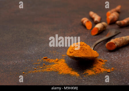 La curcuma in polvere in un vecchio cucchiaio vintage, curcuma radici su uno sfondo scuro Foto Stock