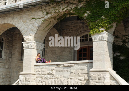 Una giovane donna legge un libro seduti sulla veranda della sala di Ontario Building, Queen's University, Kingston, Ontario, Canada. Foto Stock