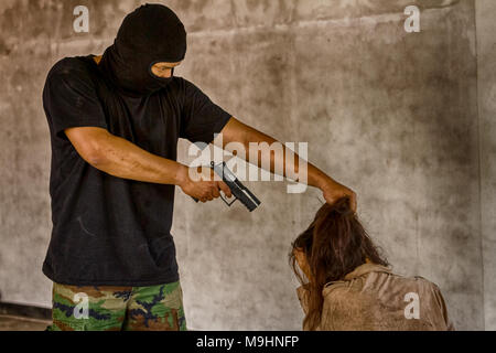 Un terrorista uomo in maschera tenendo la pistola il rapimento di donne giovani per un ostaggio in edificio abbandonato. Foto Stock