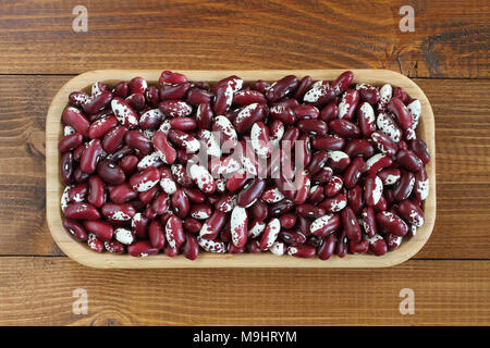 Materie rosso con bianco screziato fagioli kidney in bambù piastra su sfondo di legno Foto Stock