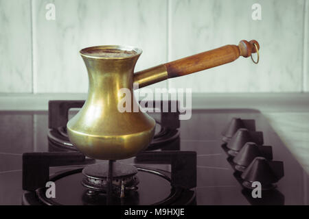 La cottura del caffè su un fornello a gas. Vecchio turco paiolo in rame per preparare il caffè sulla stufa in cucina. La colazione anticipata. Bagno turco metodo di preparazione del caffè. Foto Stock