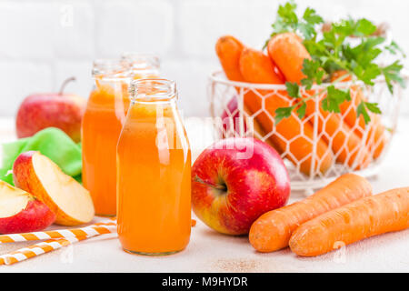 Carota fresco e succo di mela su sfondo bianco. Carota e succo di mela in bottiglie di vetro sul tavolo bianco, primo piano Foto Stock