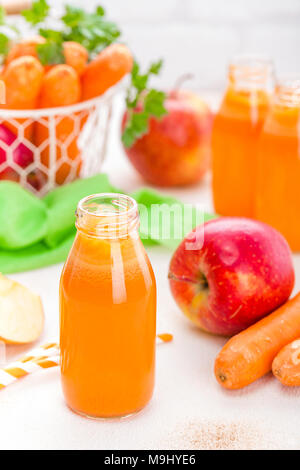 Carota fresco e succo di mela su sfondo bianco. Carota e succo di mela in bottiglie di vetro sul tavolo bianco, primo piano Foto Stock