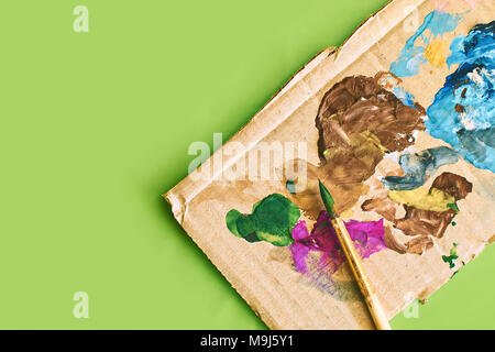 Semplice cartoncino con macchie di vernice utilizzata come la palette per la pittura e un pennello di luce verde e fresco stile di primavera sullo sfondo Foto Stock