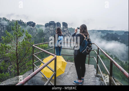 La ragazza prende una foto del suo amico al telefono sulla roccia e guarda alle montagne, Cielo e nubi in una piovosa giornata d'estate. Telaio orizzontale. Foto Stock