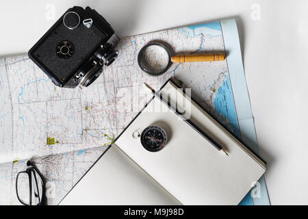 La realizzazione di un piano di viaggio. Mappa, vuoto notepad, fotocamera, Magnifier, bussola, matita e bicchieri. Lay piatto. Foto Stock