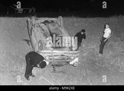 Un poliziotto indaga su una vettura che ha rotolato giù da un terrapieno in California, ca. 1960. Foto Stock