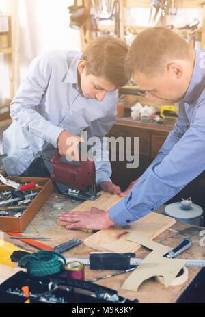 Ritratto di padre e figlio il taglio di tavolato in legno con Seghetto da traforo nel luogo di lavoro Foto Stock