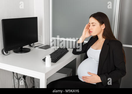 Donna incinta con mal di testa in ufficio. La gravidanza, imprenditrice, lavoro, stress, gestosi concetto. Madre in attesa sensazione di malessere sul posto di lavoro. Pneumatico Foto Stock