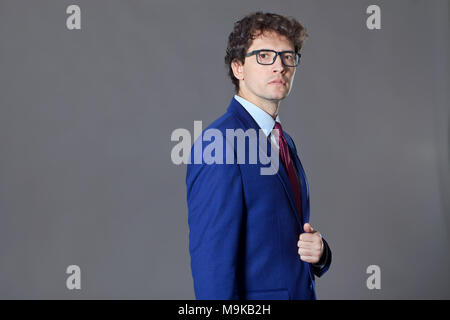 Giovani seriamente man standing ang mantenendo la sua giacca blu Foto Stock