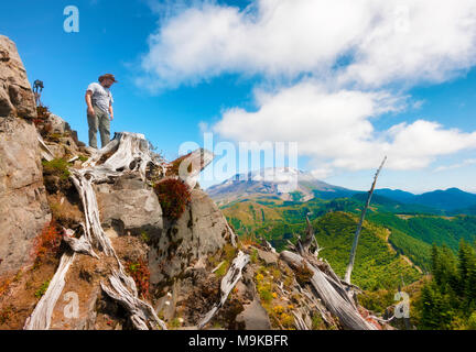 Un escursionista/fotografo guarda verso il basso dalla parte superiore della Cima del Castello, il suo cavalletto e fotocamera vicino con Mt. Sant Helens in background in Gifford Pinchot Na Foto Stock