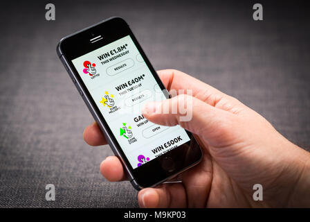 Un uomo con la lotteria nazionale app su un iPhone Foto Stock