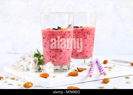 Mirtillo frullati di frutti di bosco, banana e mandorle in bicchieri con cocktail di tubi su un bianco tavola di legno Foto Stock