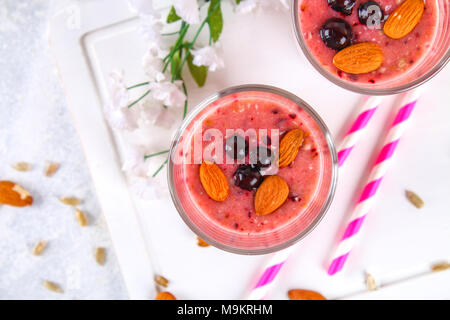 Mirtillo frullati di frutti di bosco, banana e mandorle in bicchieri con cocktail di tubi su un bianco tavola di legno Foto Stock