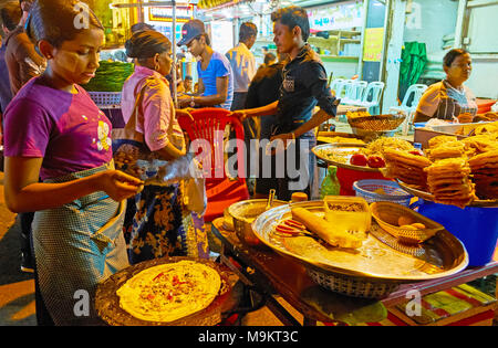 YANGON, MYANMAR - Febbraio 14, 2018: ragazza giovane cuochi tradizionale birmana street food - frittelle con le verdure e i ceci fritti croccanti torte, Mah Foto Stock