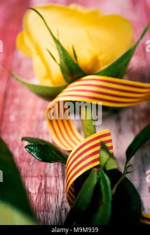 Una rosa gialla e una bandiera catalana su un rustico di una superficie di legno per Sant Jordi, il nome catalano per Saint Georges giorno, quando è tradizione per dare le rose Foto Stock