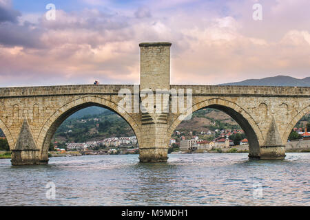 Coppia giovane tenendo selfie su antiche, iconico Drina ponte sotto il colorato nuvole viola e azzurro cielo, fotografato dal fiume Foto Stock