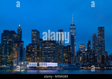 La parte inferiore di Manhattan skyline che si vede attraverso l'East River mostra le luci della città e le luci accese in Pier 17 Foto Stock