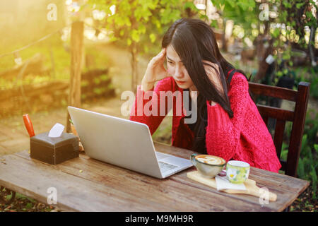 Preoccupato della donna utilizzando laptop e di bere il caffè in giardino Foto Stock