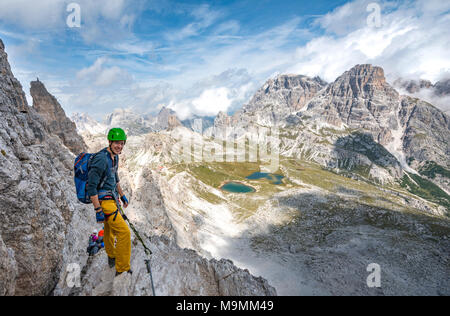 Escursionista sulla via ferrata alla Paternkofel, dietro il Lago dei Piani con Schusterplatte e Altensteinspitz, Dolomiti di Sesto Foto Stock