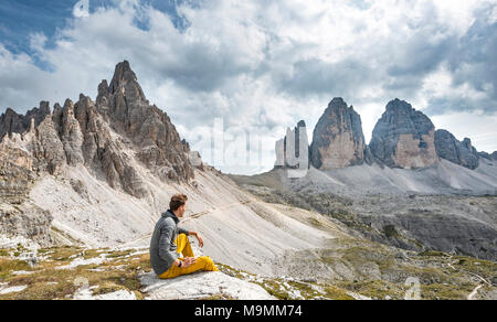 Escursionista si siede sulla roccia, vertice del Paternkofel e pareti nord delle Tre Cime di Lavaredo, Sesto Dolomiti Alto Adige Südtirol Foto Stock