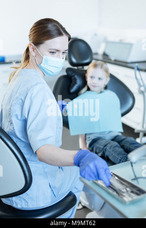 Controllo approfondito. Piacevole giovane femmina dentista di effettuare un controllo preliminare del suo piccolo paziente e la scelta di uno strumento necessario per che Foto Stock