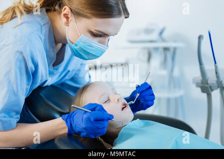 Il servizio era di buon livello. Carino petite ragazza distesa in una poltrona del dentista con gli occhi chiusi e avente i suoi denti esaminati da una cura dentista femmina tramite una bocca mi Foto Stock
