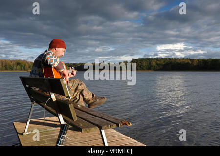 Uomo suona la chitarra su un pontile di sbarco al lago, Meclemburgo Lake District, Meclemburgo-Pomerania Occidentale, Germania Foto Stock