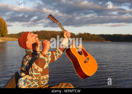 Uomo suona la chitarra su un pontile di sbarco presso il lago ed è lieta, Meclemburgo Lake District, Meclemburgo-Pomerania Occidentale Foto Stock