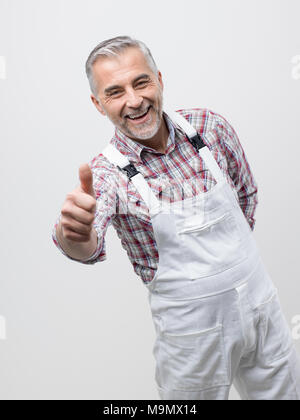 Sorridente pittore professionale in salopette da dare un pollice in alto Foto Stock