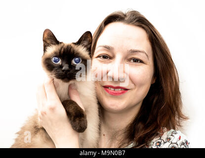 Bella donna con il gatto siamese gatto nelle sue braccia sorriso per la fotocamera Foto Stock