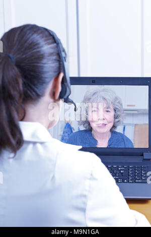 Medico donna della geriatria con la cuffia nella parte anteriore del suo portatile nel corso di una consultazione su internet con un paziente senior, concetto di telemedicina Foto Stock