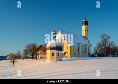 Facciata, guglie e il tetto dell'Wilparting barocca chiesa di pellegrinaggio e la cappella contro il cielo blu in winterlandscape nevoso di sunrise, Bavaria Foto Stock