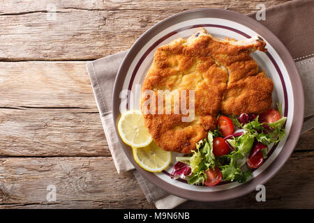 Milanese di vitello con limone e insalata fresca di pomodori e lattuga close-up su una piastra. parte superiore orizzontale vista da sopra Foto Stock