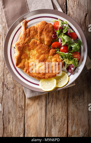 Milanese di vitello con limone e insalata fresca di pomodori e lattuga close-up su una piastra. Verticale in alto vista da sopra Foto Stock