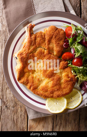 Deliziosa Costoletta di vitello alla milanese con limone e una fresca insalata di verdure close-up su una piastra. Verticale in alto vista da sopra Foto Stock