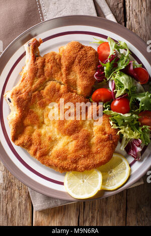 Vitello milanese (cotoletta alla milanese) con limone e una fresca insalata di verdure close-up su una piastra. Verticale in alto vista da sopra Foto Stock