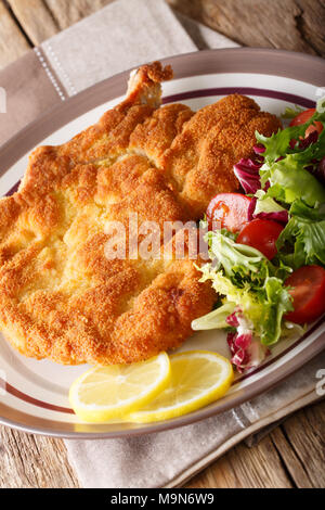 Milanese di vitello con limone e insalata fresca di pomodori e lattuga close-up su una piastra. In verticale Foto Stock