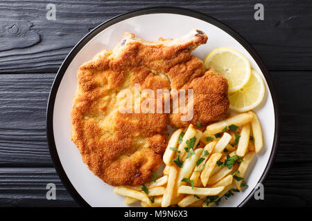 Fried Costoletta di vitello alla milanese con limone e patatine fritte close-up su una piastra. parte superiore orizzontale vista da sopra Foto Stock