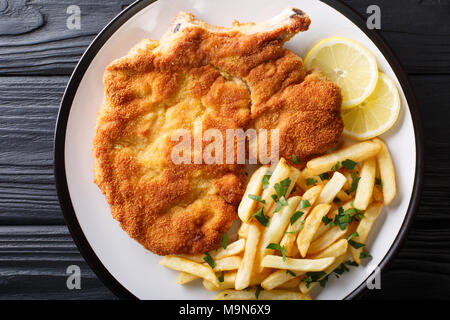 Carne di vitello alla milanese (cotoletta alla milanese con patatine fritte close-up su una piastra su un tavolo. horizontall vista in pianta da sopra Foto Stock