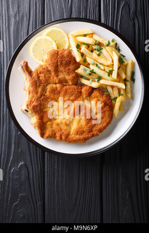 Tradizionale Italiana Milanese di vitello con limone e patatine fritte close-up su una piastra. Verticale in alto vista da sopra Foto Stock