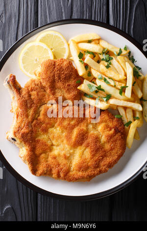 Carne di vitello alla milanese (cotoletta alla milanese con patatine fritte close-up su una piastra su un tavolo. Verticale in alto vista da sopra Foto Stock