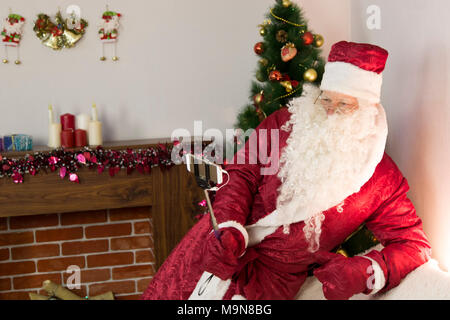 In camera vicino all'albero di Natale, Babbo Natale è in possesso di un self-stick e farsi le foto in modi diversi. Foto Stock