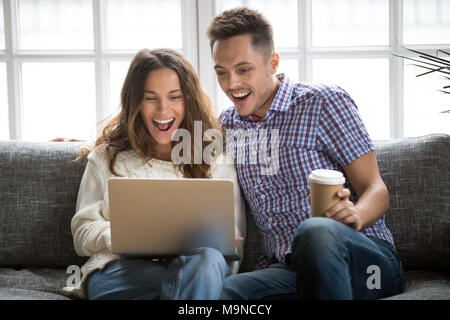 Emozionato coppia giovane guardando lo schermo del notebook seduti a casa sul divano, sorpreso allegro uomo e donna felice con buone notizie on line, stupito da speciali Foto Stock