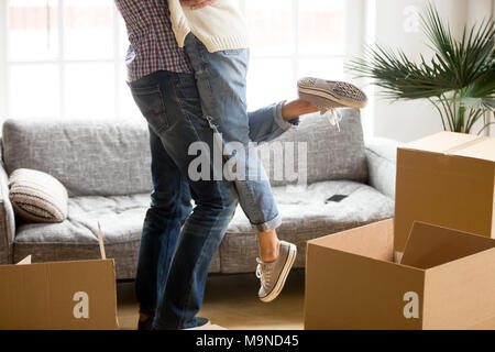 Coppia felice sul giorno del trasloco concetto, sollevamento uomo donna in piedi tra le scatole di cartone a partire vivere insieme in una nuova casa marito holding embrac Foto Stock