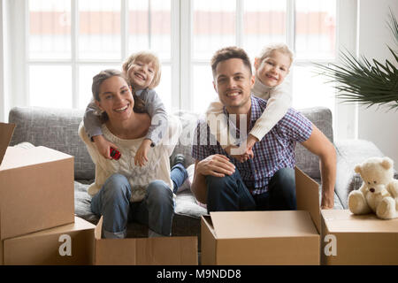 Ritratto di felice multinazionale giovane famiglia bonding insieme sorridente adottato i bambini che abbraccia i genitori sul lettino con scatole sul giorno del trasloco, bambini uova rotte Foto Stock