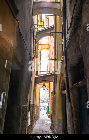 Stretto vicolo buio in un italiano medievale città tradizionale con luce proveniente dalla fine, porte sulle pareti laterali e lanterna appeso al di sotto di un arco Foto Stock