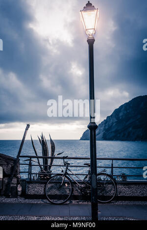 Via lampada lanterna accesa al tempo della sera illuminando un percorso panoramico con vista sul mare e sulla costa. Noleggio parcheggiato dietro di esso. Foto Stock