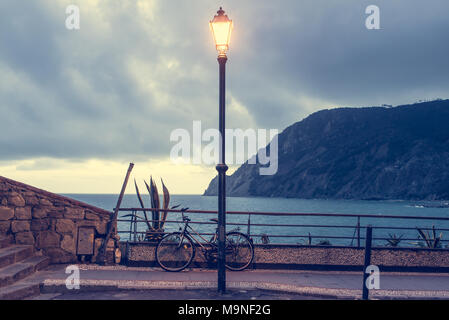 Via lampada lanterna accesa al tempo della sera illuminando un percorso panoramico con vista sul mare e sulla costa. Noleggio parcheggiato dietro di esso. Vintage effetto opaco Foto Stock