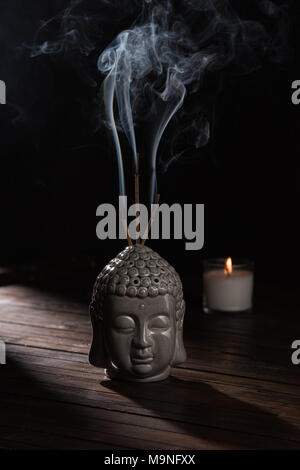 La scultura della testa del budda con la masterizzazione di bastoncini di incenso e candela sul tavolo Foto Stock